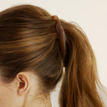 Close-up of a woman wearing a honey-coloured banana clip in their ponytail against a neutral background