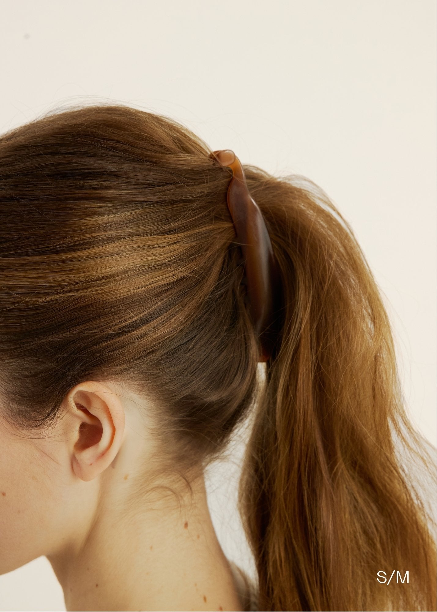 Close-up of a woman wearing a honey-coloured banana clip in their ponytail against a neutral background