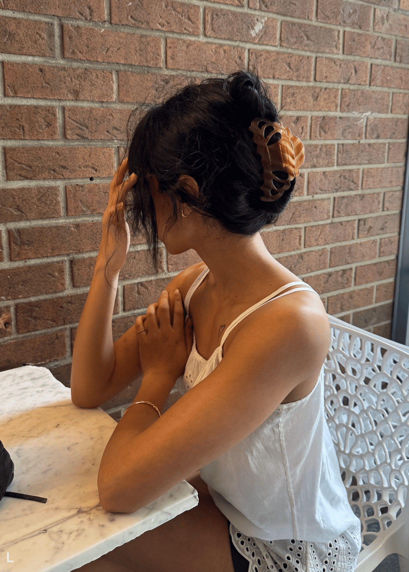 Woman sitting on a bench with a brick wall background wearing a large caramel-coloured hair clip.