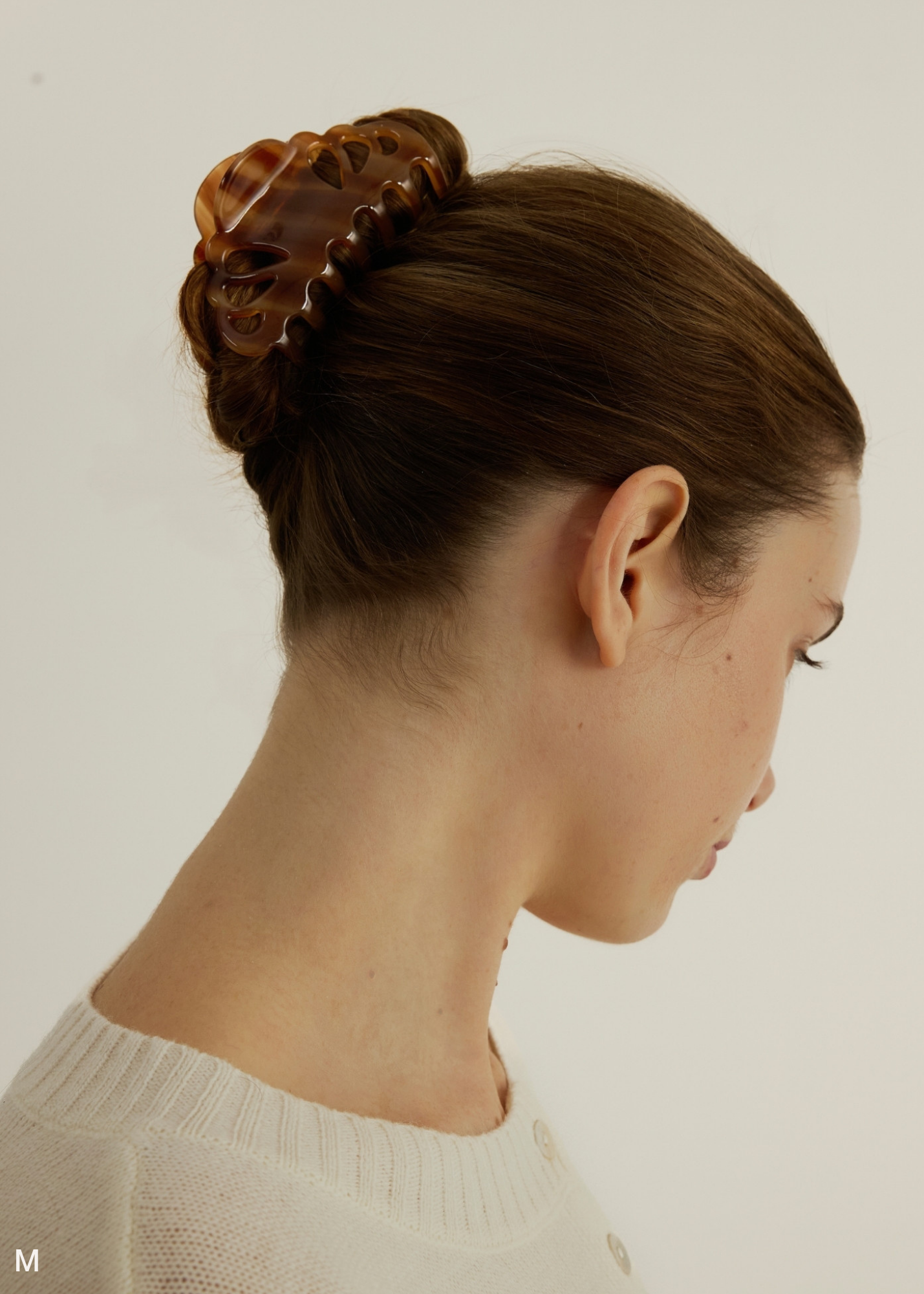 Woman with a caramel coloured, medium-sized hair clip in her hair against a plain background
