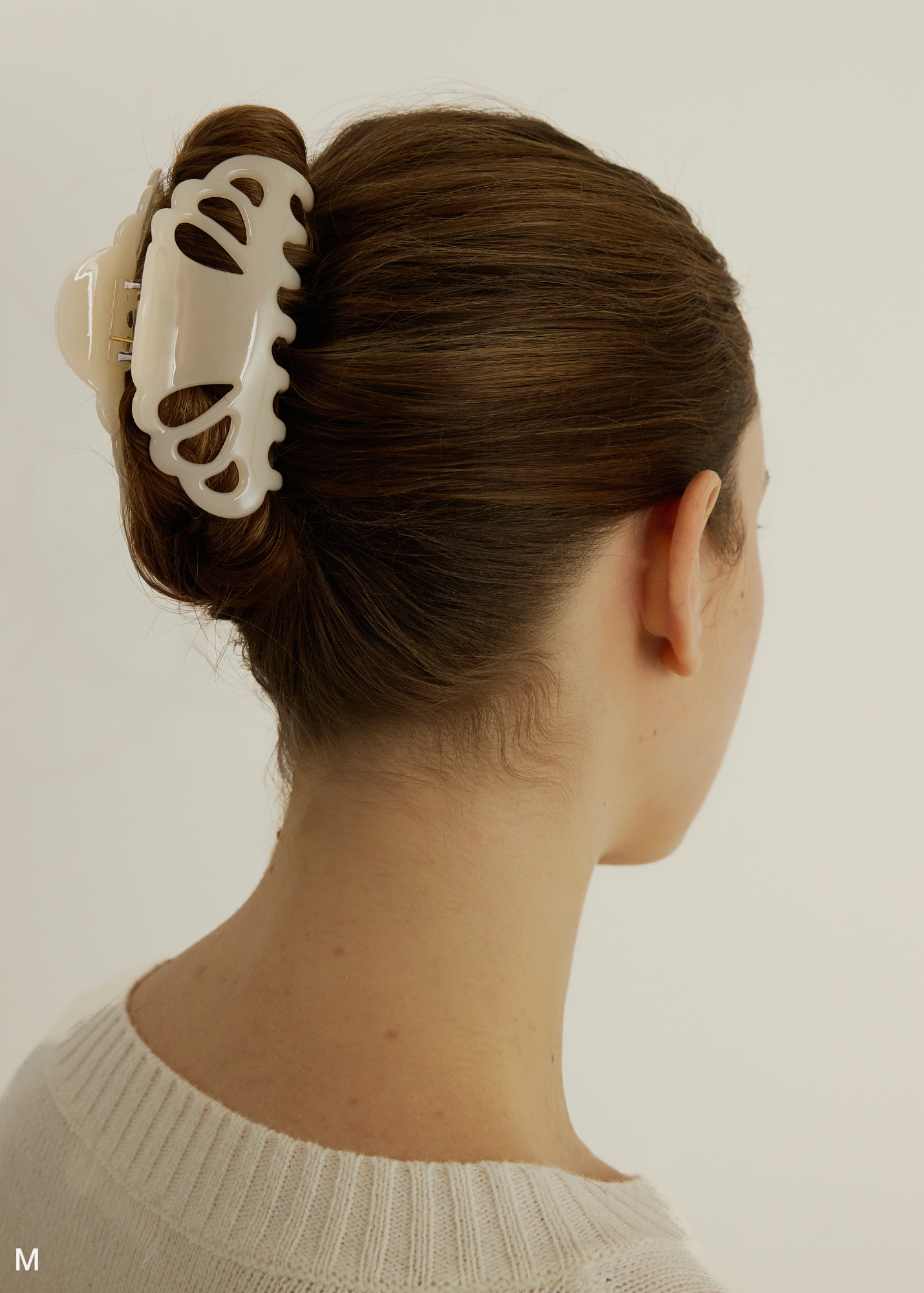 Woman with brown hair styled in an updo with a cream-coloured medium-sized claw clip against a plain background