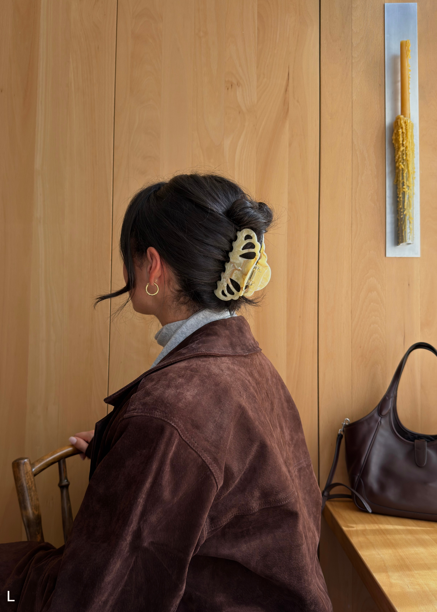 Person with a hair clip standing against a wooden wall with a handbag on a bench.