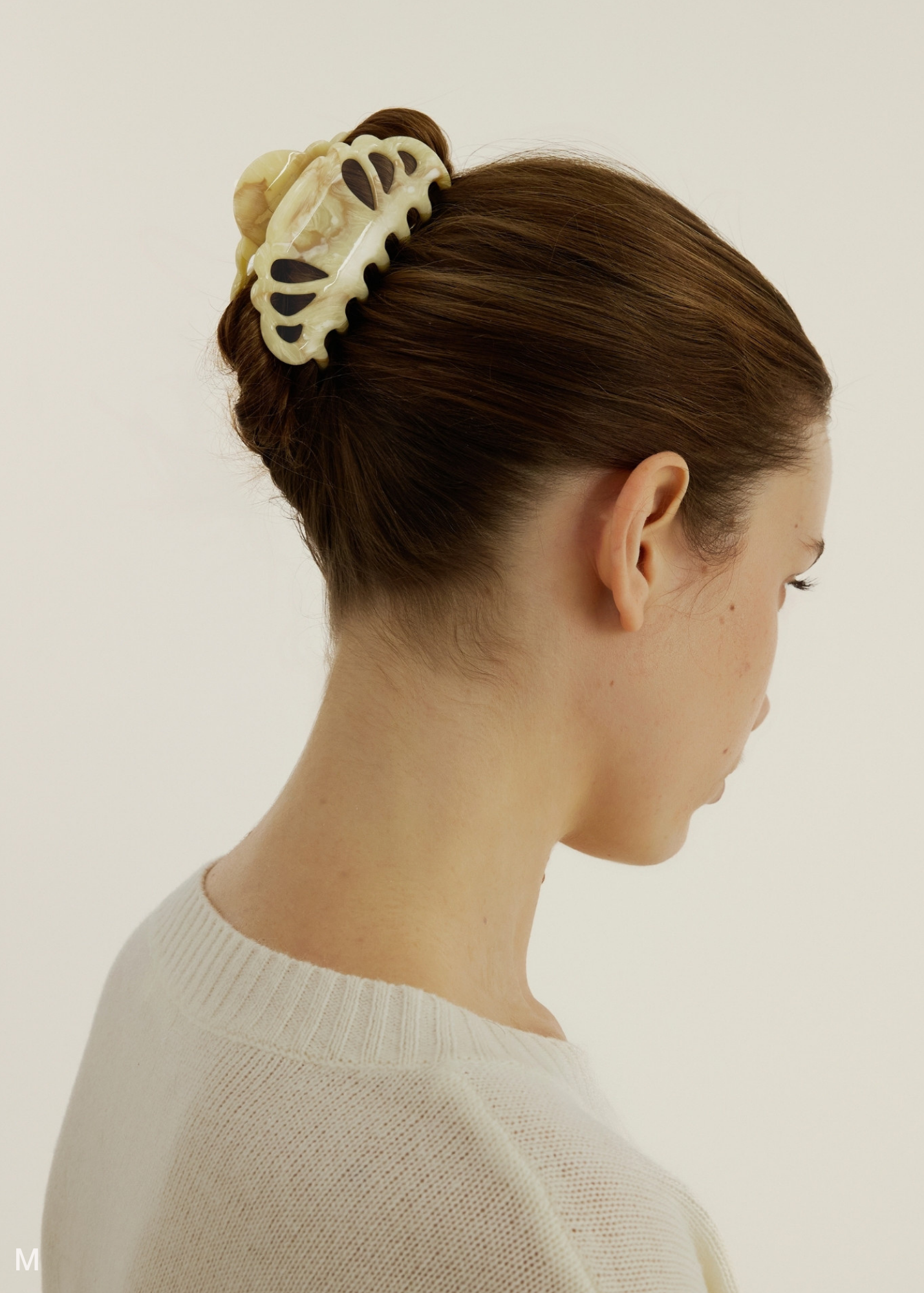 Woman with a beige hair clip on a plain background.