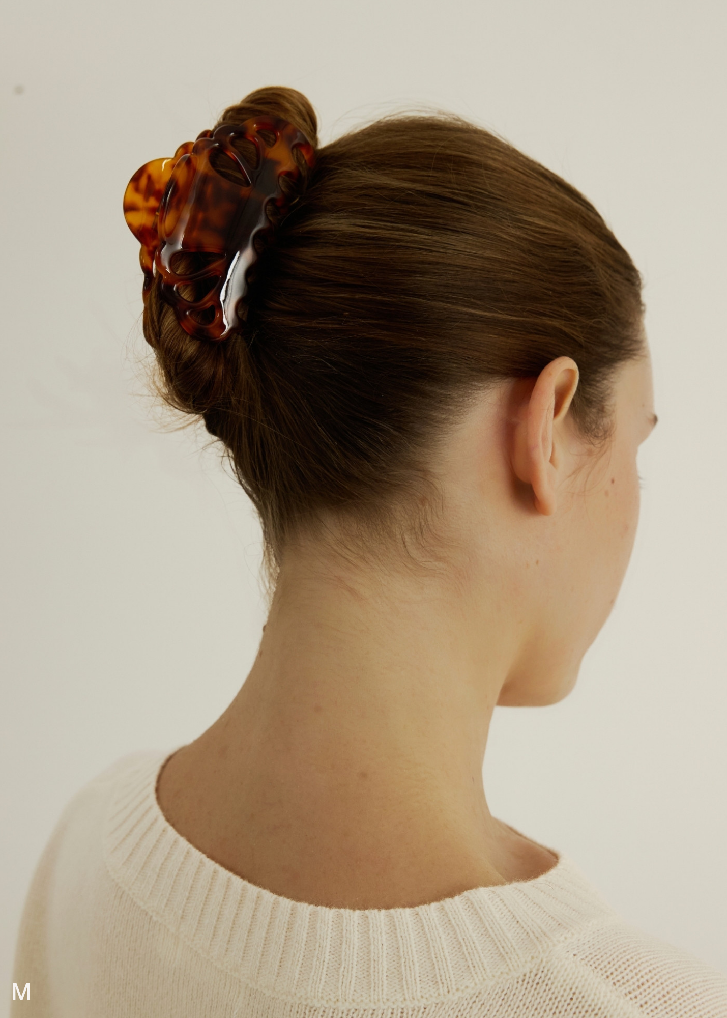 Person with a bun and tortoiseshell hair clip on a plain background