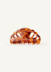A tortoise-coloured hair claw clip with scalloped edges and tear drop shaped cut outs on a white background