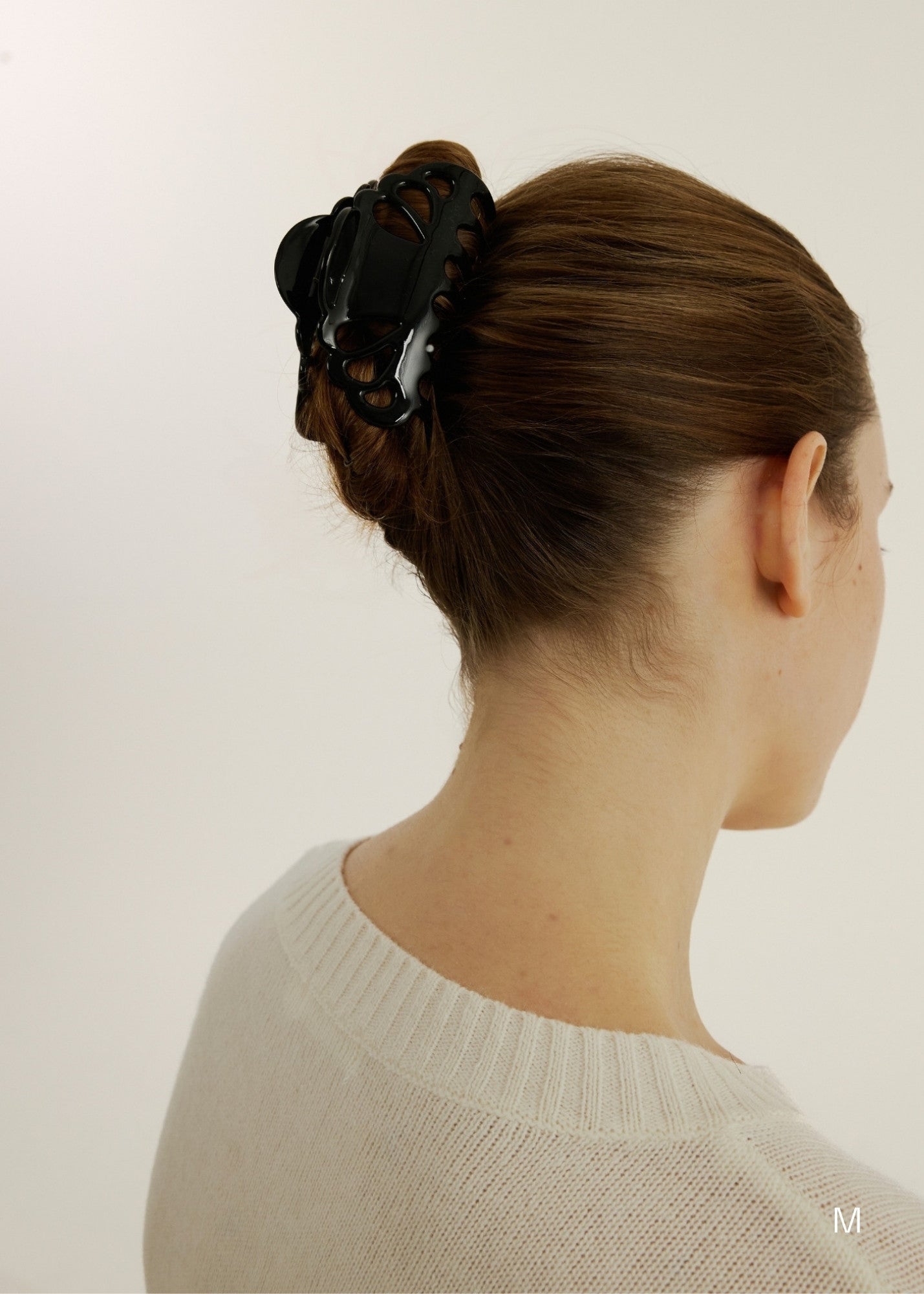 Woman with hair in an up-do hairstyle secured with a medium black hair claw clip with scalloped edges and tear drop shaped cut outs wearing a white top
