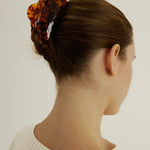 Woman with hair in an up-do hair style secured with a tortoise coloured hair claw clip that has scalloped edges and tear drop shaped cut outs wearing a white tank top.