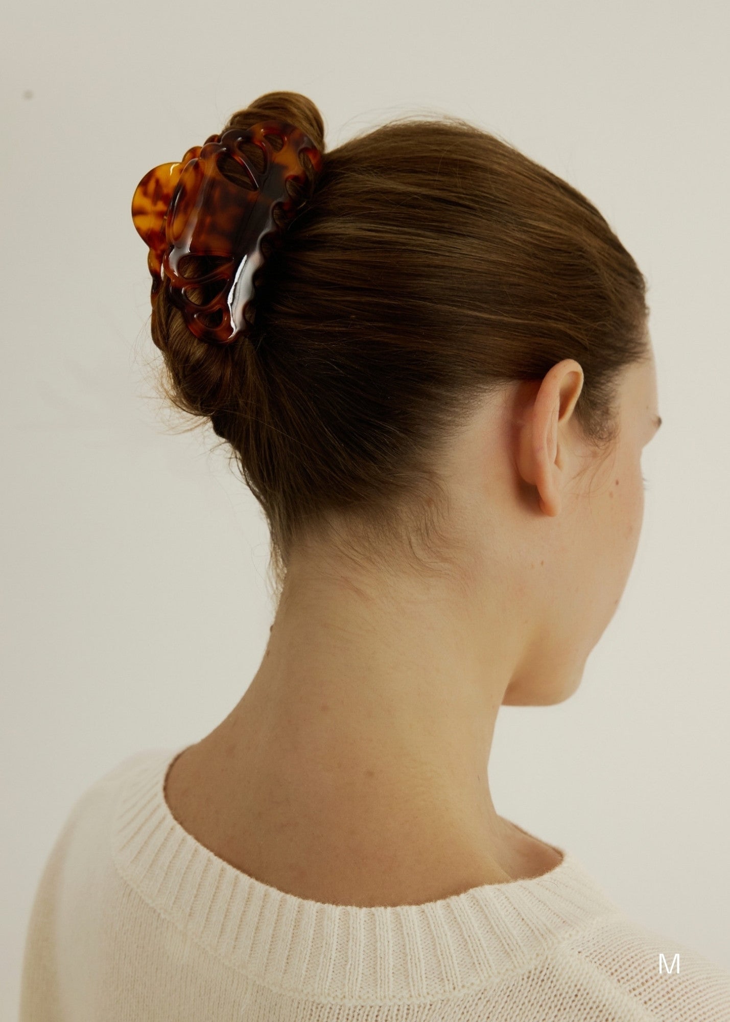 Woman with hair in an up-do hair style secured with a tortoise coloured hair claw clip that has scalloped edges and tear drop shaped cut outs wearing a white tank top.