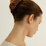 Woman with brown hair styled in an updo secured with a honey-coloured decorative claw clip on a plain background