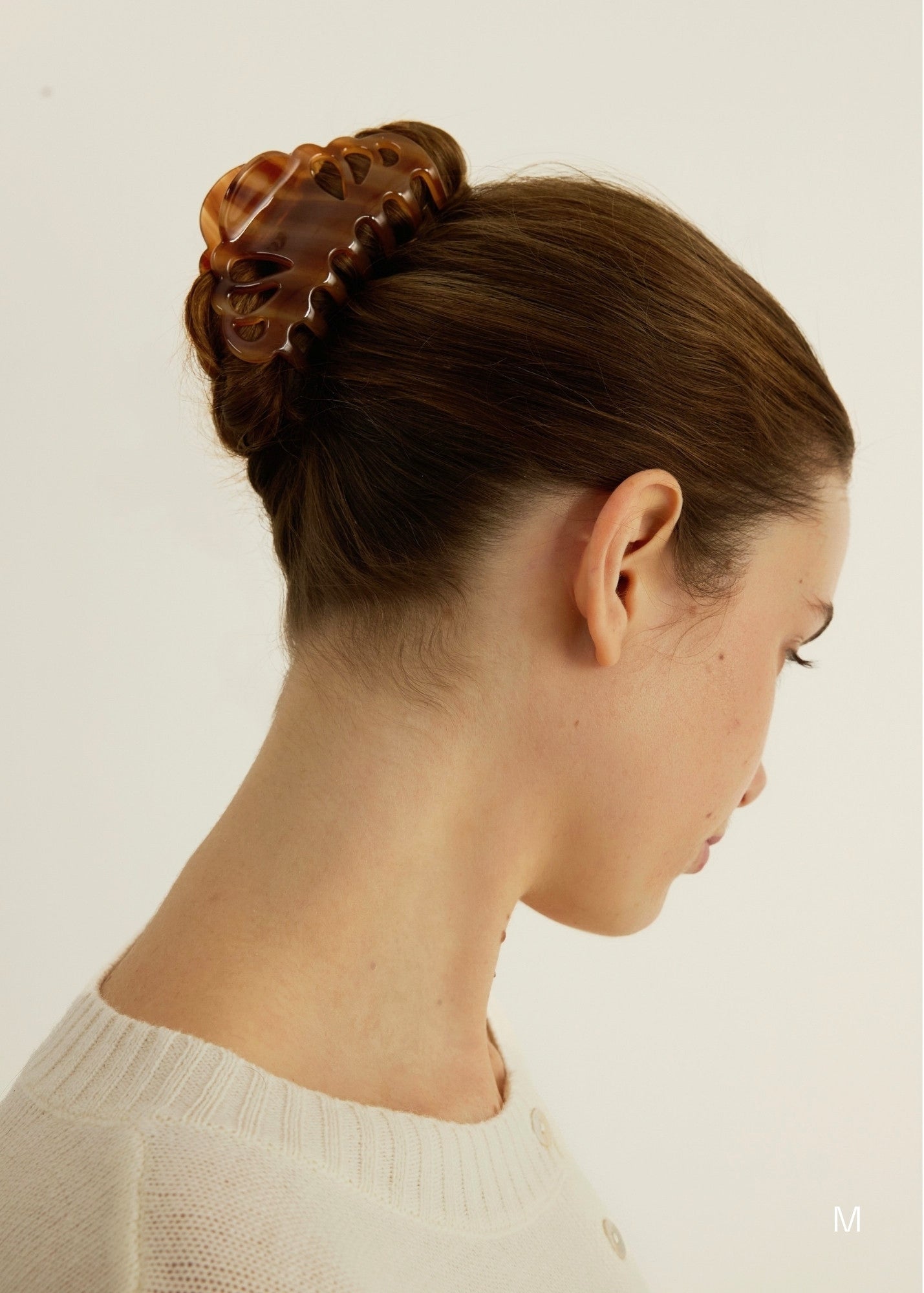 Woman with brown hair styled in an updo secured with a honey-coloured decorative claw clip on a plain background