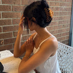 Woman with dark hair styled with a large honey-coloured decorative claw clip sitting on a bench with a brick wall background