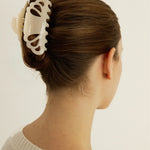 Woman with brown hair styled in an updo with a cream-coloured medium-sized claw clip against a plain background