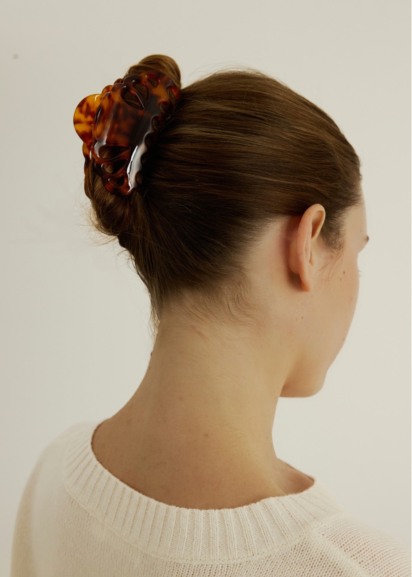 Woman with hair in an up-do hair style secured with a tortoise coloured hair claw clip that has scalloped edges and tear drop shaped cut outs wearing a white tank top.