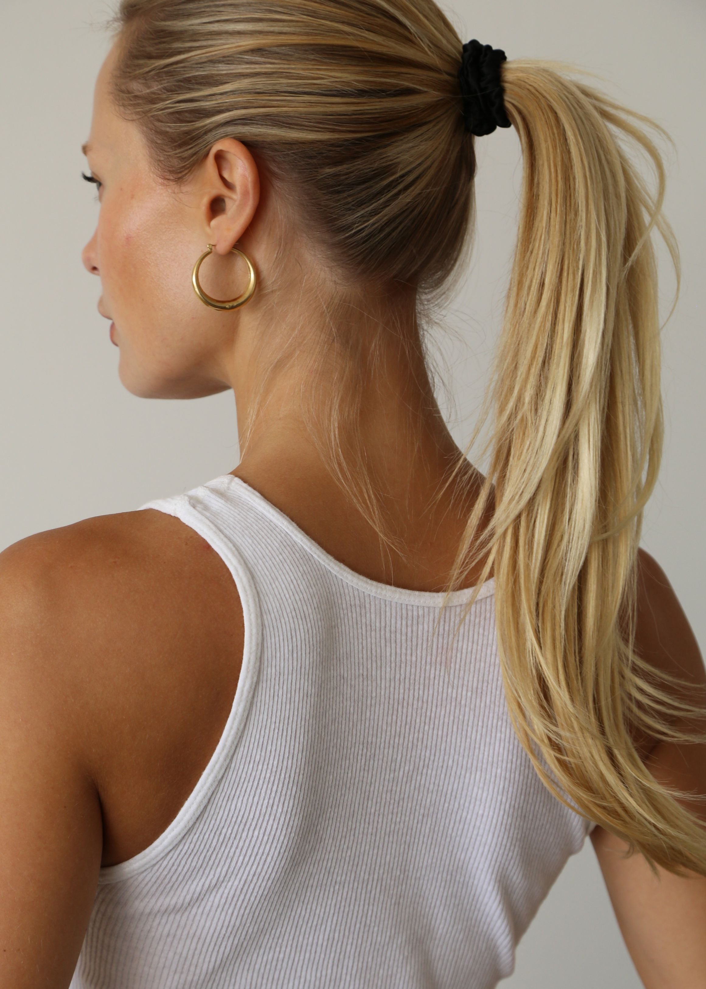 Woman with blonde hair styled in a ponytail secured with the silk hair tie in black