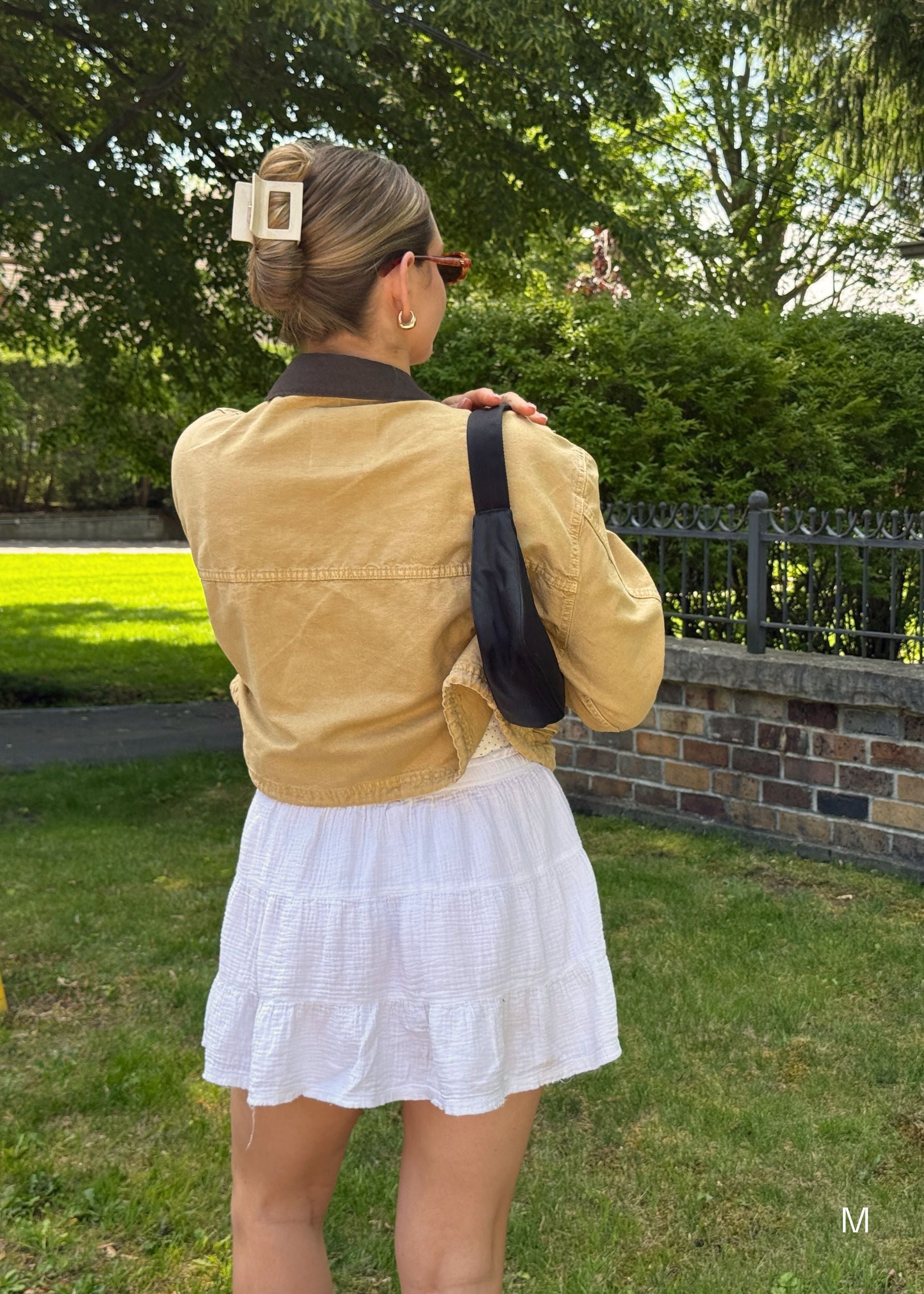 Person wearing a jacket and white skirt with a black bag, standing outdoors showing their up-do hairstyle with a medium sized beige hair clip