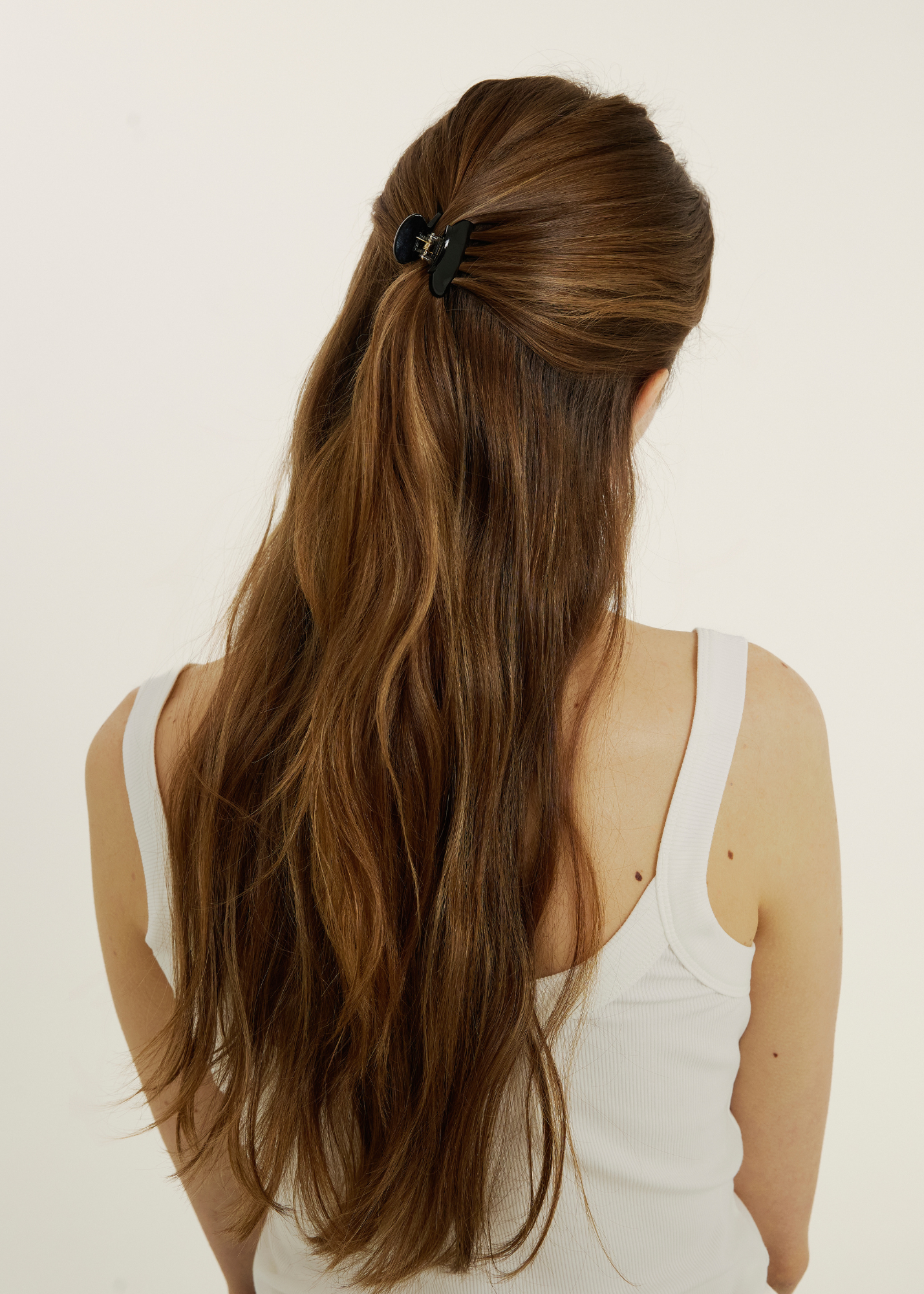Person with long brown hair secured half up with a black mini claw clip on a plain background.