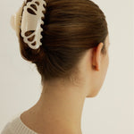 A woman with brown hair styled in an up-do hairstyle secured with a cream coloured hair clip in their bun against a plain background