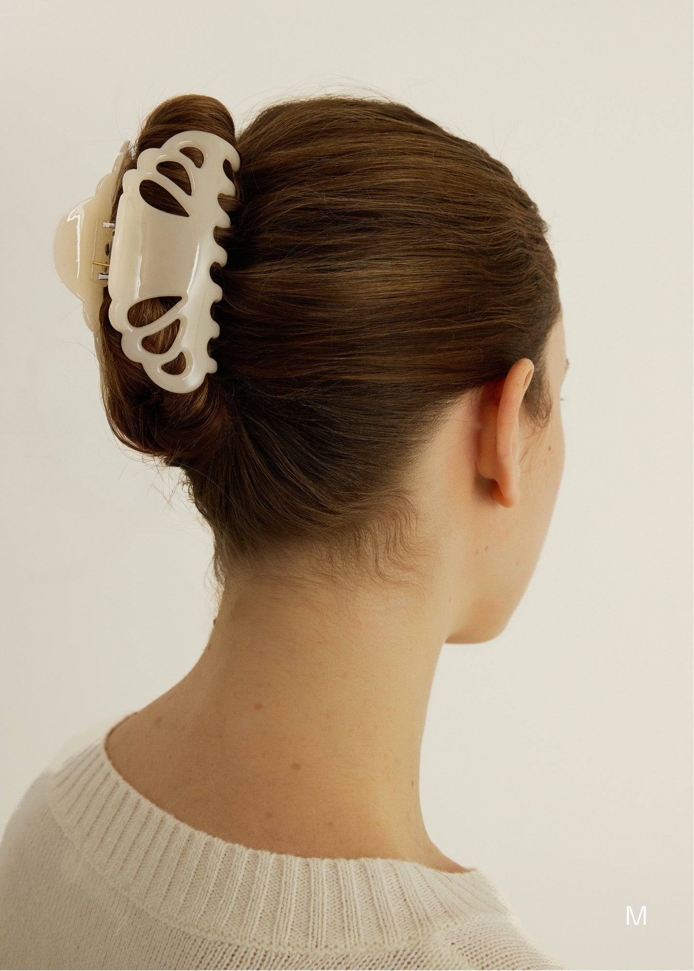 A woman with brown hair styled in an up-do hairstyle secured with a cream coloured hair clip in their bun against a plain background