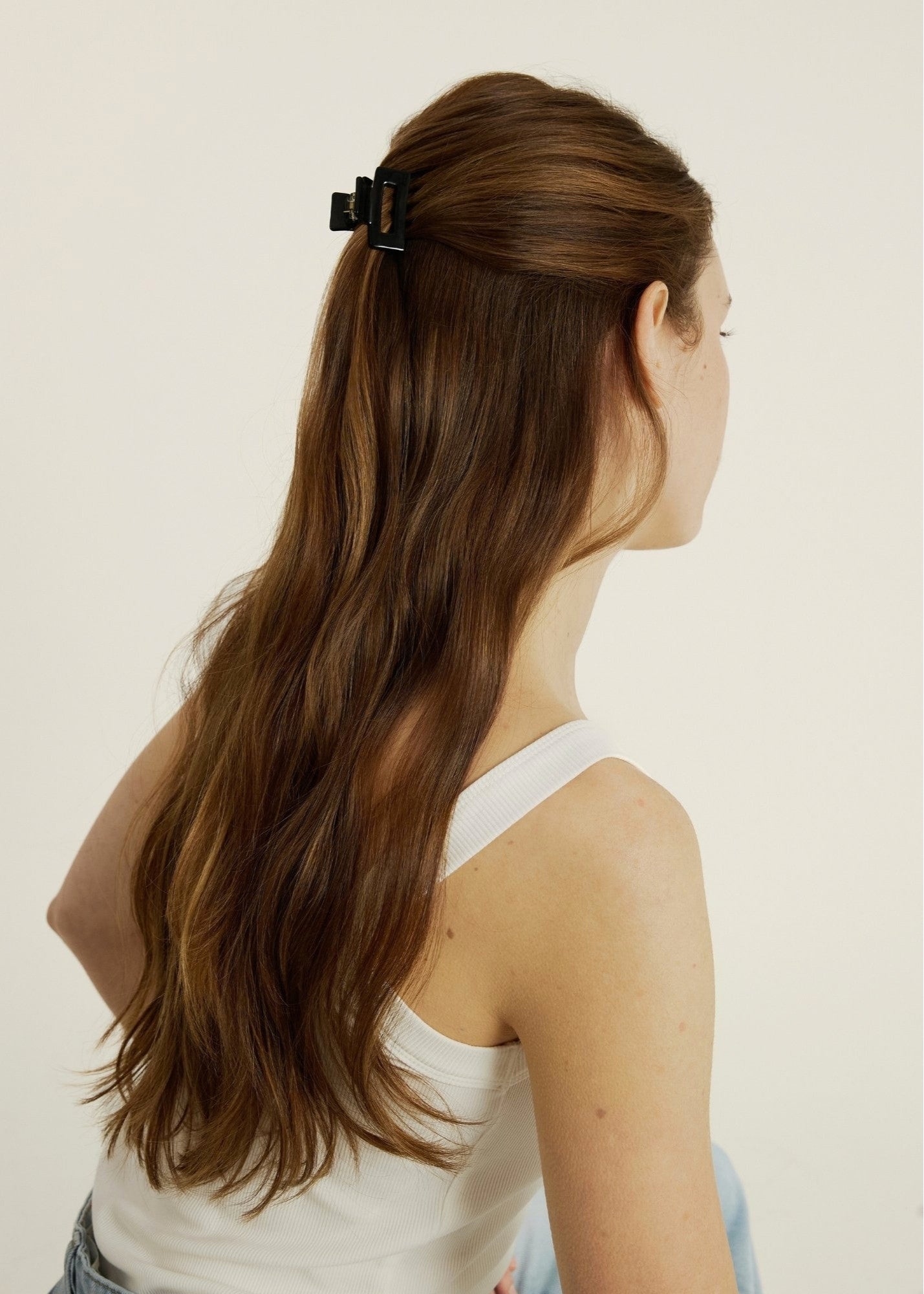 Woman with long brown hair wearing a mini black hair clip on a plain background