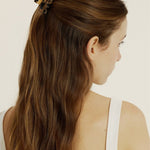 Woman with long brown hair styled half-up, half-down secured with a mini hair clip wearing a white tank top against a plain background