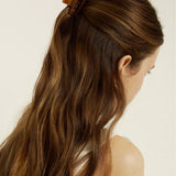Woman with long brown hair wearing a mini honey-coloured hair clip against a neutral background