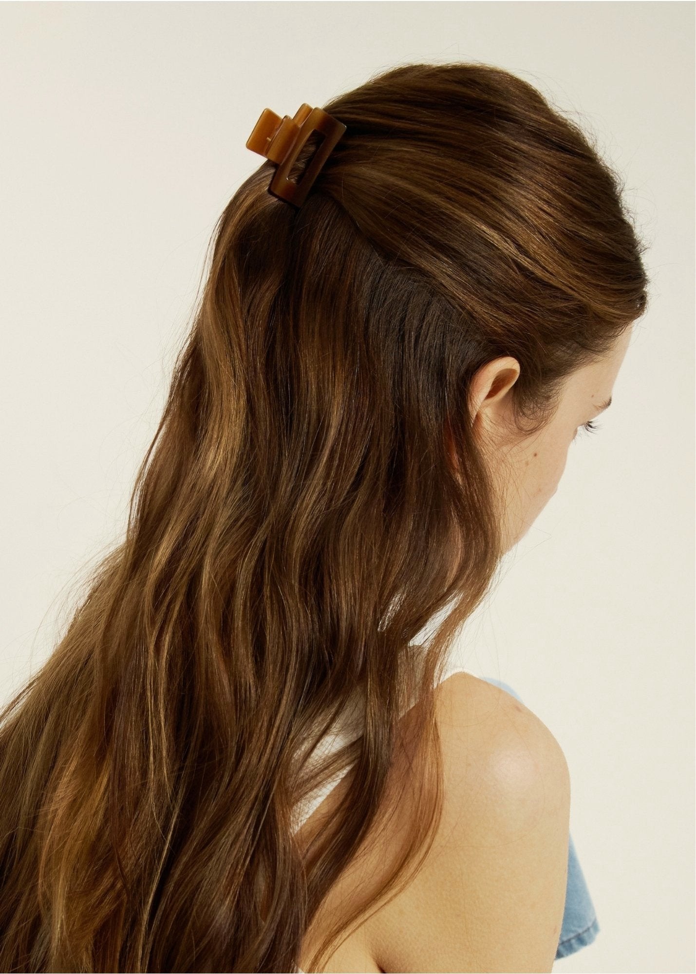 Woman with long brown hair wearing a mini honey-coloured hair clip against a neutral background