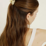 Woman with long brown hair styled in a ponytail with a minil beige-coloured hair clip, wearing a white tank top.