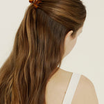Woman with long brown hair styled in a ponytail with a mini tortoise-coloured hair clip, wearing a white tank top.