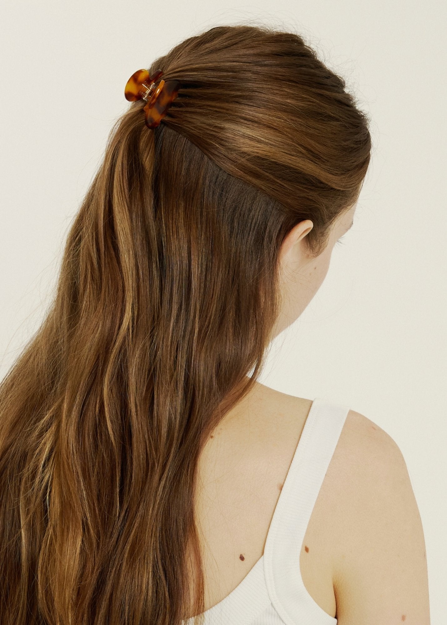 Woman with long brown hair styled in a ponytail with a mini tortoise-coloured hair clip, wearing a white tank top.