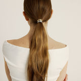 Woman with long hair tied in a ponytail with the mixed metal hair cuff, wearing a white top on a plain background
