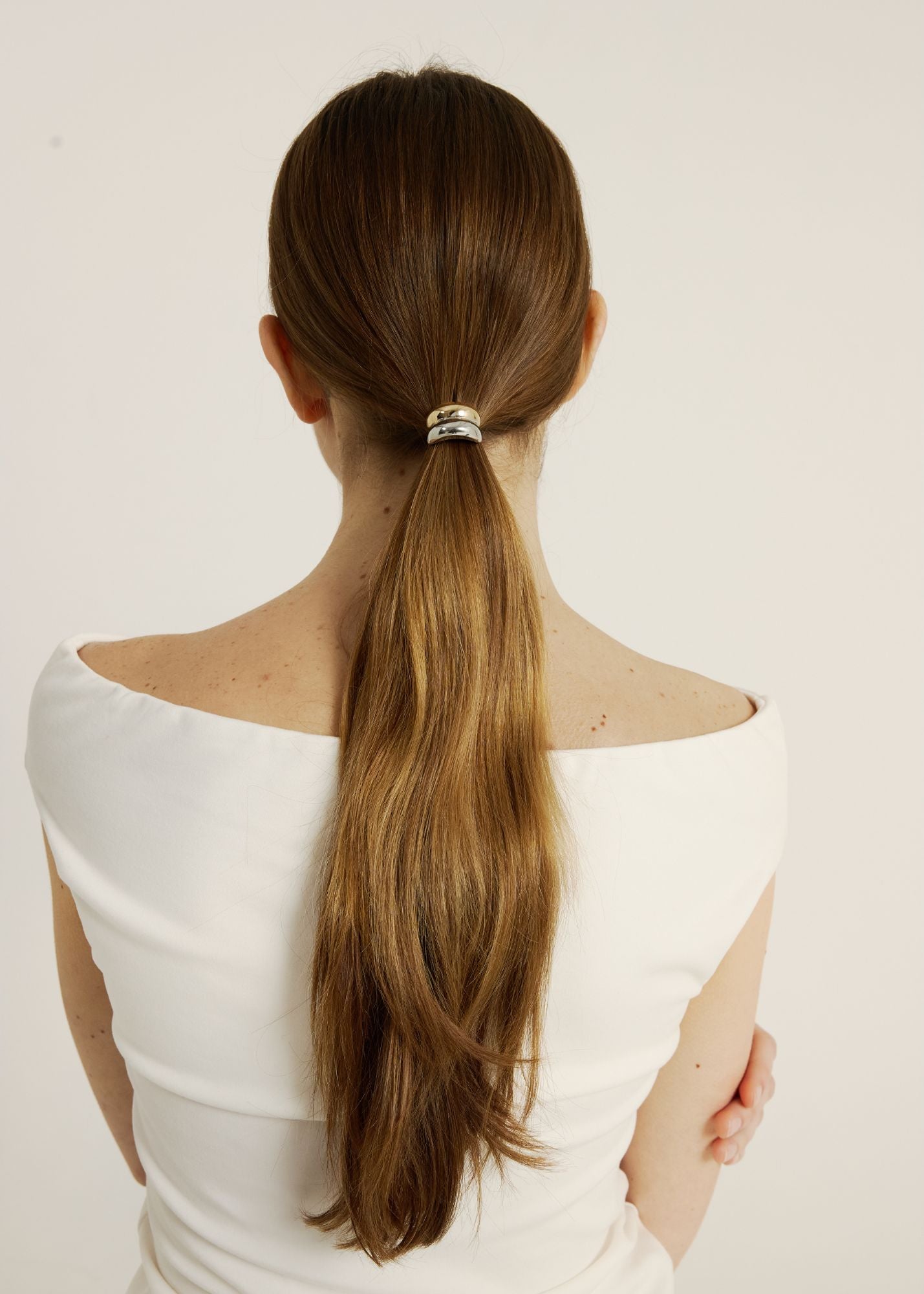 Woman with long hair tied in a ponytail with the mixed metal hair cuff, wearing a white top on a plain background