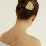 Back view of a woman with a hair bun secured with a beige coloured, decorative claw clip against a plain background