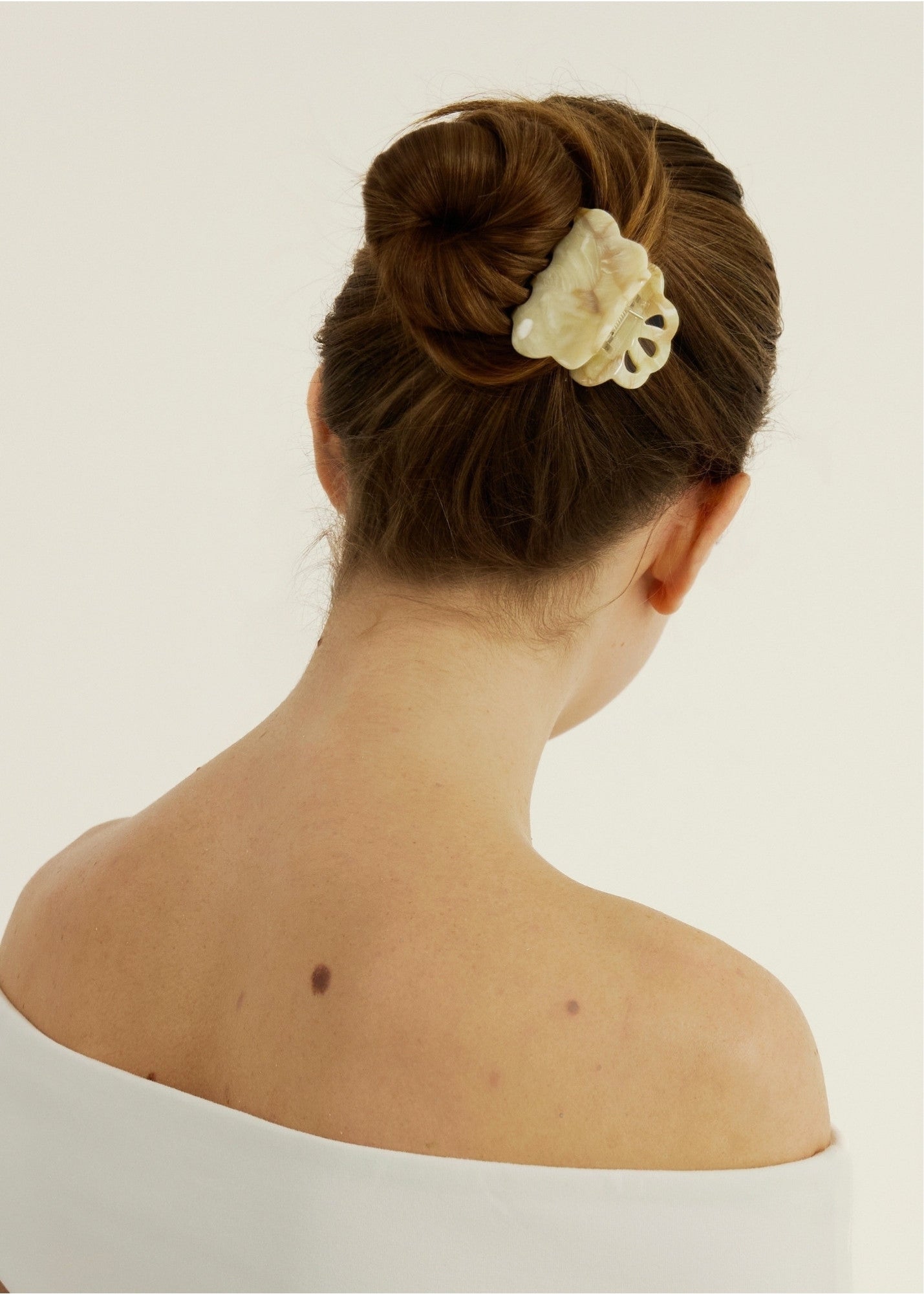 Back view of a woman with a hair bun secured with a beige coloured, decorative claw clip against a plain background