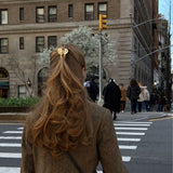 Woman with long brown hair wearing a small beige-coloured hair clip crossing a city street.