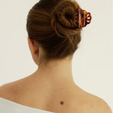 Back view of a woman with a bun secured with a decorative tortoise-coloured hair clip on a plain background