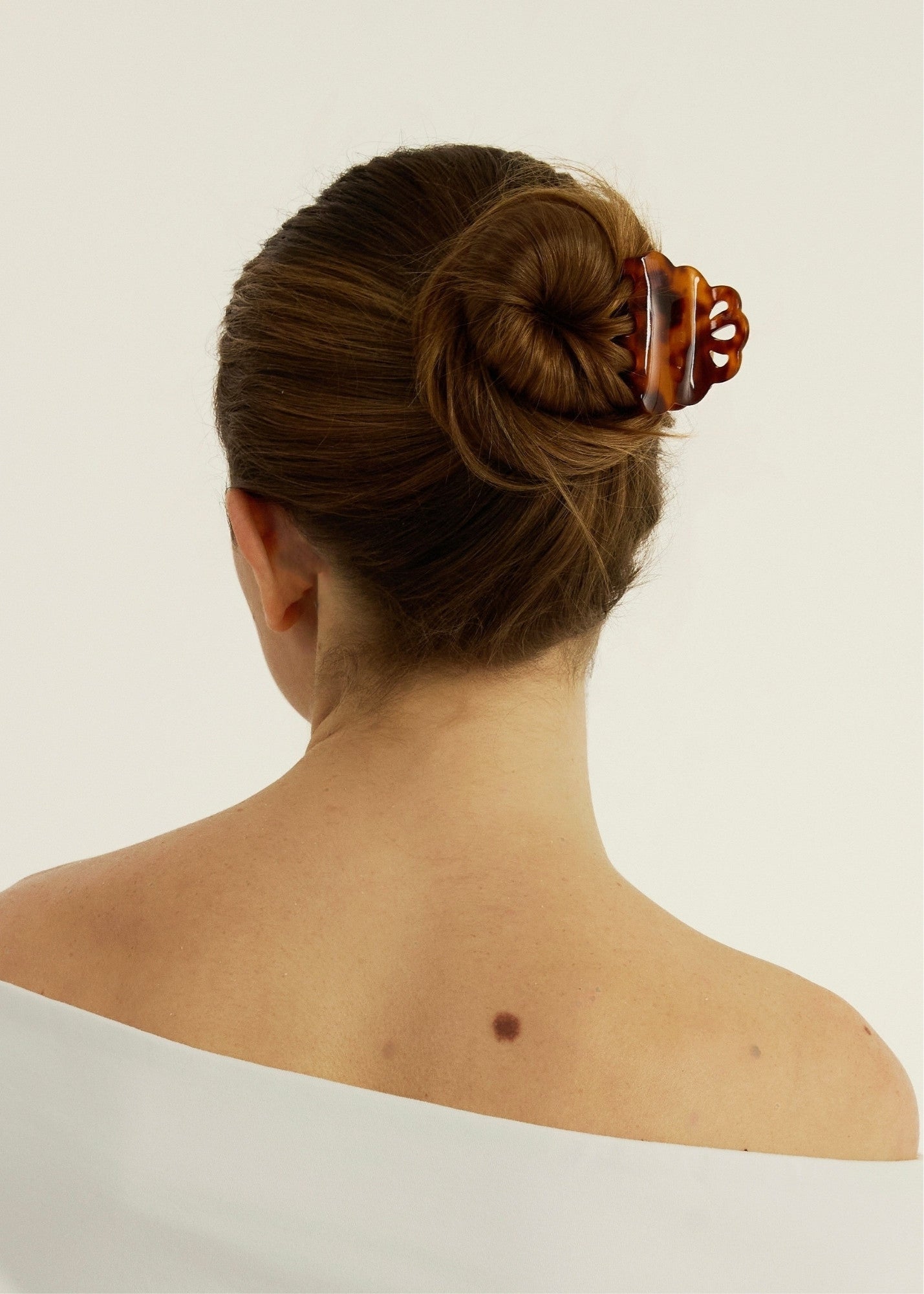 Back view of a woman with a bun secured with a decorative tortoise-coloured hair clip on a plain background