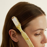 Woman with a hairbrush in her hair taming fly-aways against a plain background