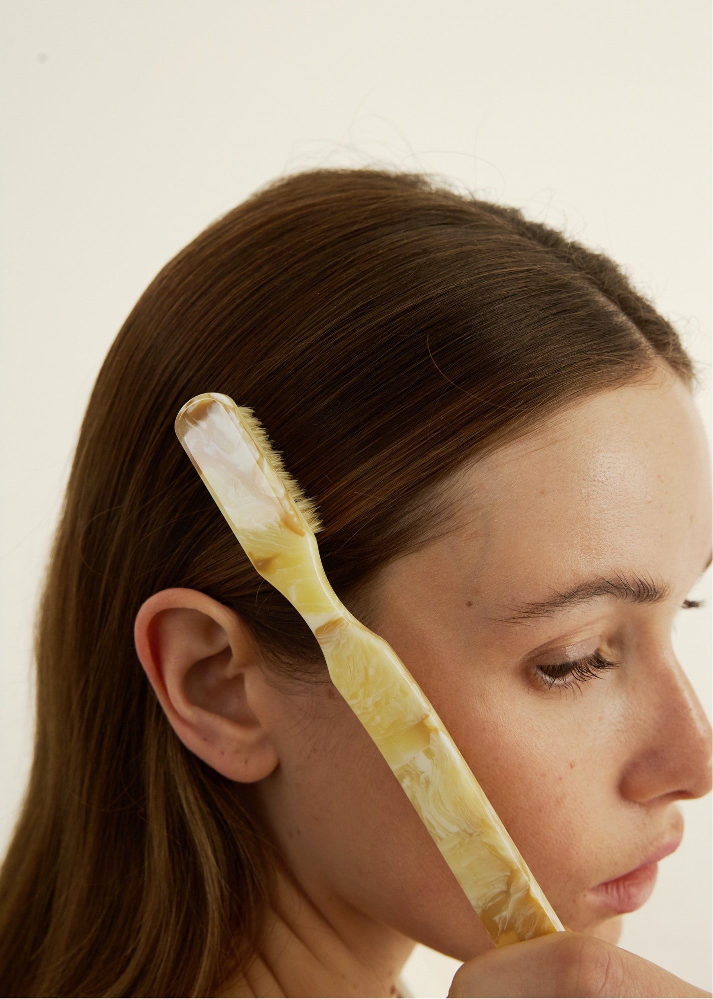 Woman with a hairbrush in her hair taming fly-aways against a plain background