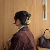Woman with dark hair styled with a beige coloured claw clip, sitting in a room with wooden walls and a handbag on a bench.