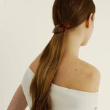 Woman with long brown hair secured back with a tortoise-coloured barrette against a plain background