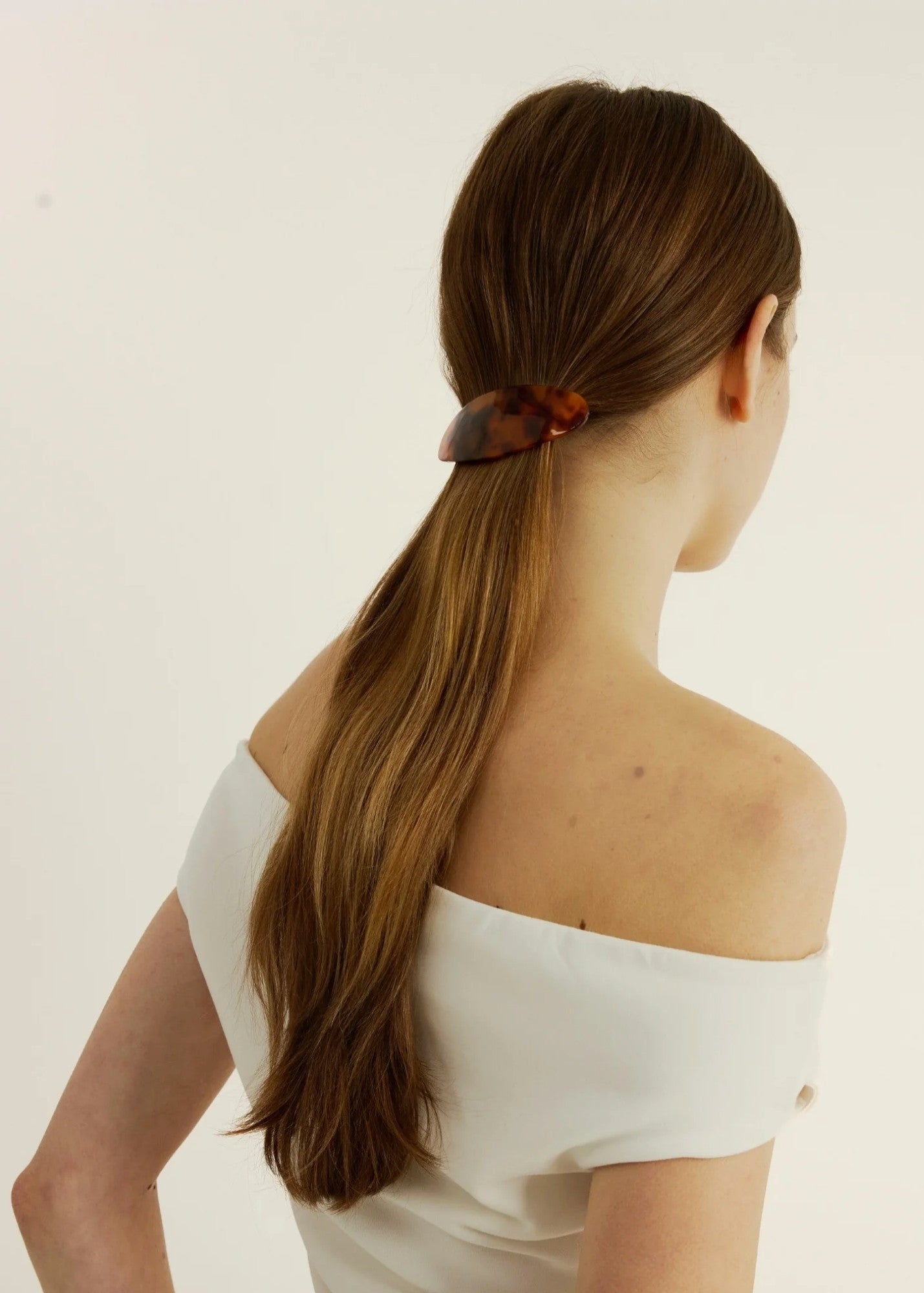 Woman with long brown hair secured back with a tortoise-coloured barrette against a plain background