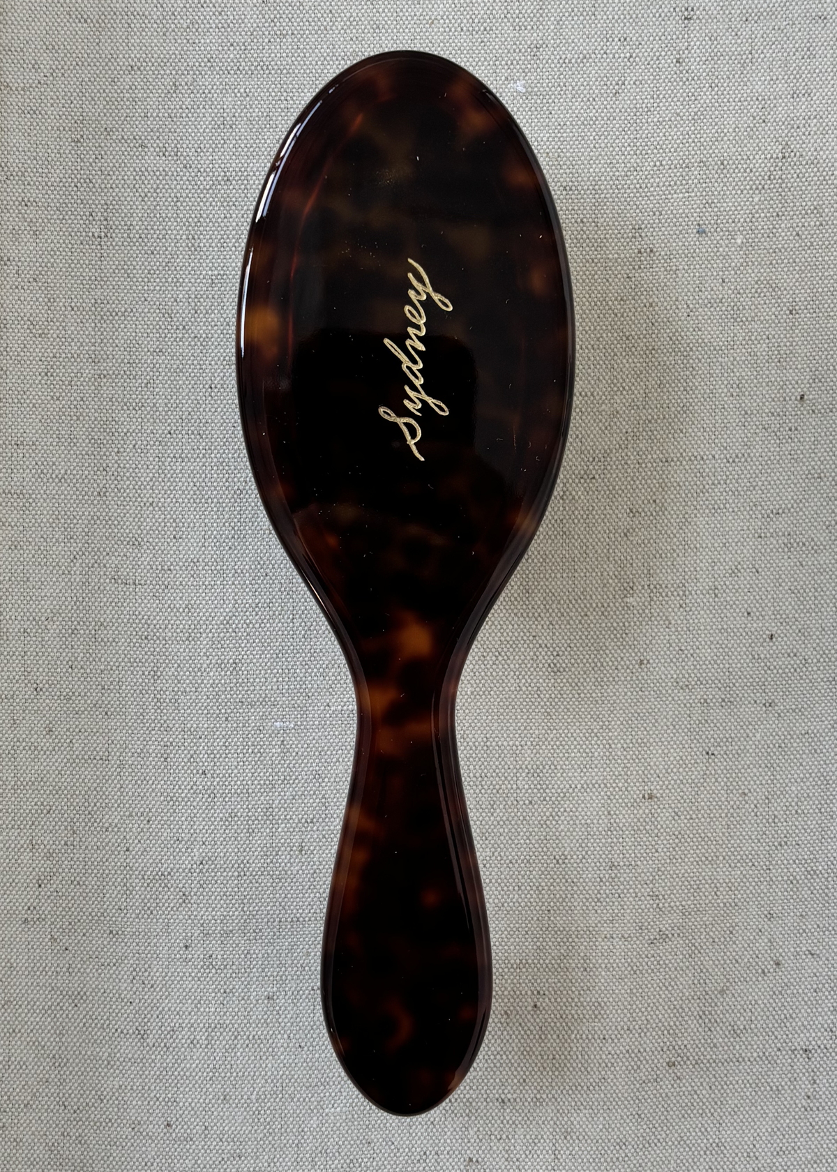 Tortoise-coloured hairbrush with 'Sydney' engraved in gold on a gray fabric background