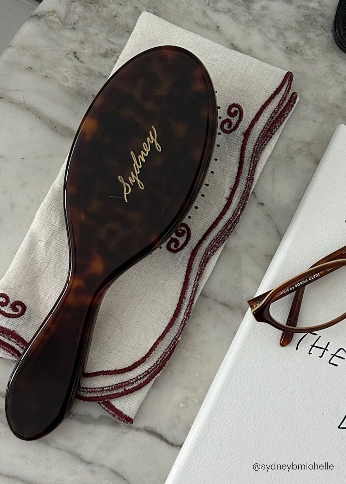 The Refine Hairbrush in Tortoise with 'Sydney' engraved on the brush and on a marble surface