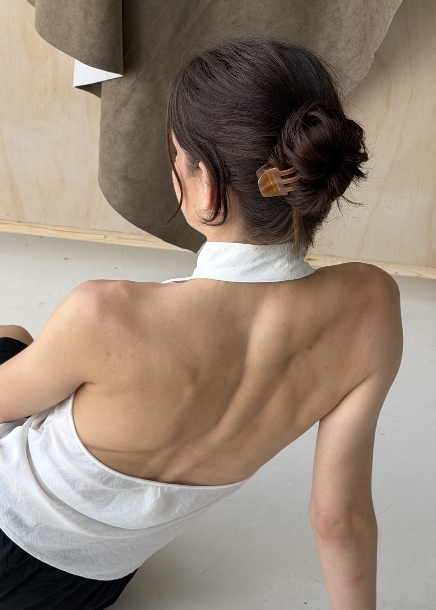 Person with their hair in a bun secured by a caramel coloured hair clip, sitting on the ground.