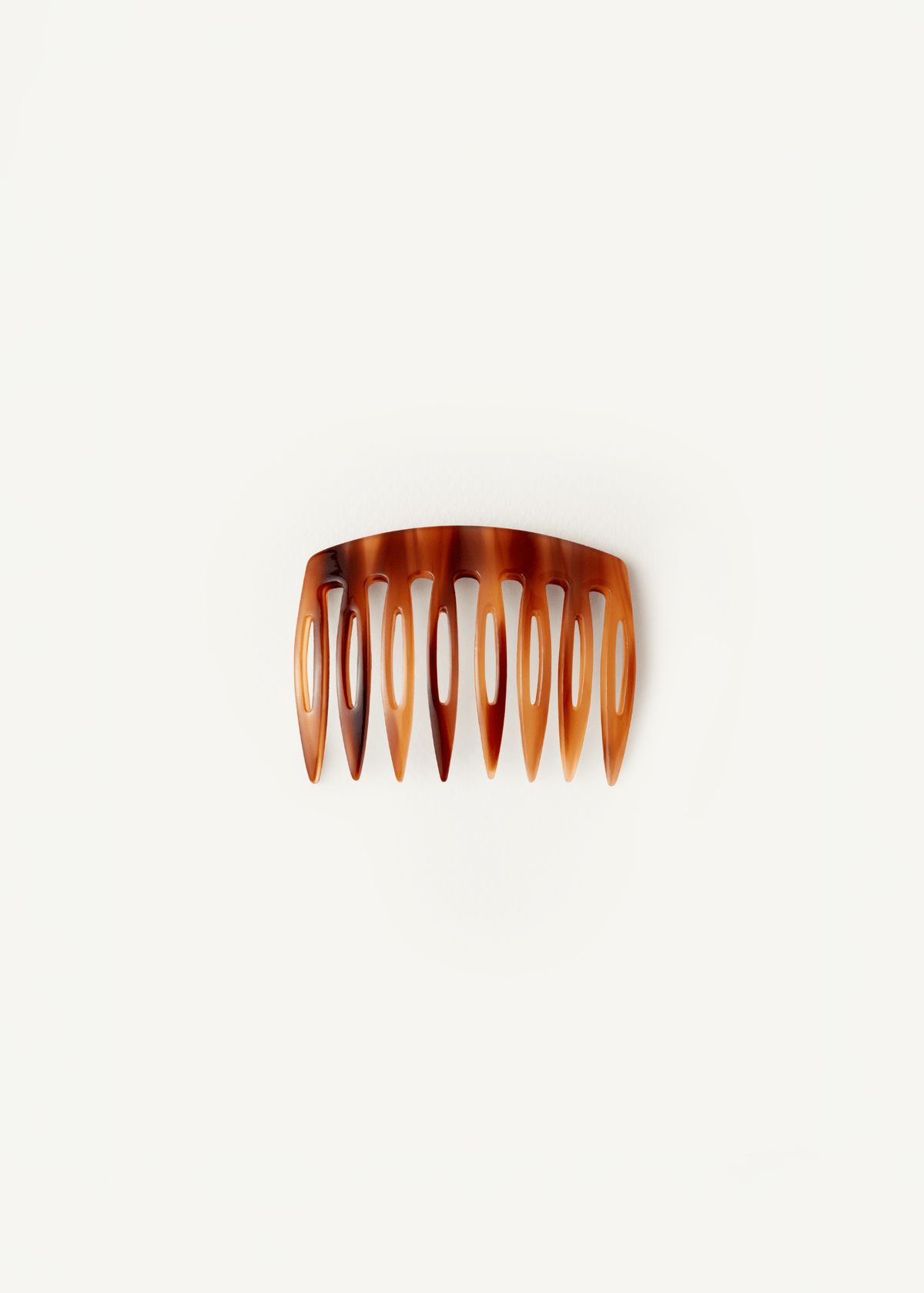 A small, slightly curved comb in an amber brown pattern against a neutral background
