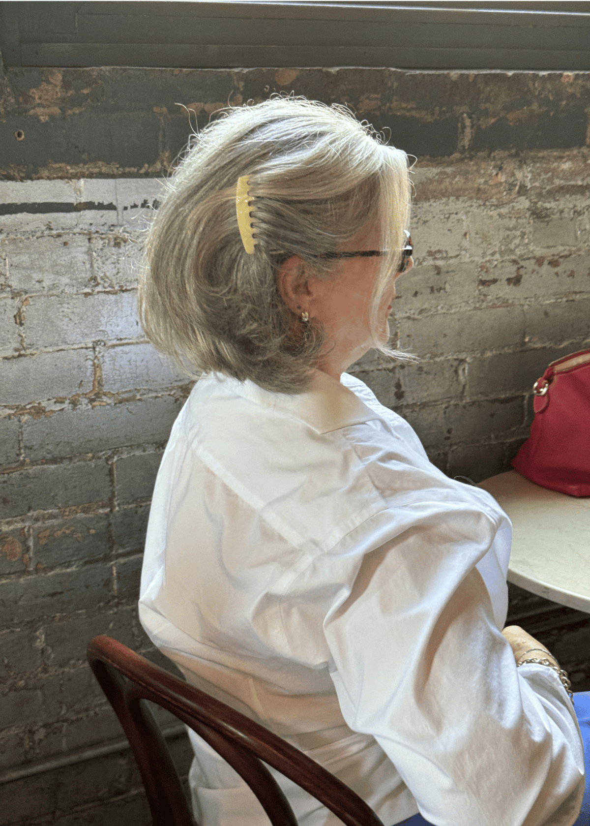 A woman in profile with jaw-length grey hair. Her hair is swept back to the side and secured using a light neutral hair comb.