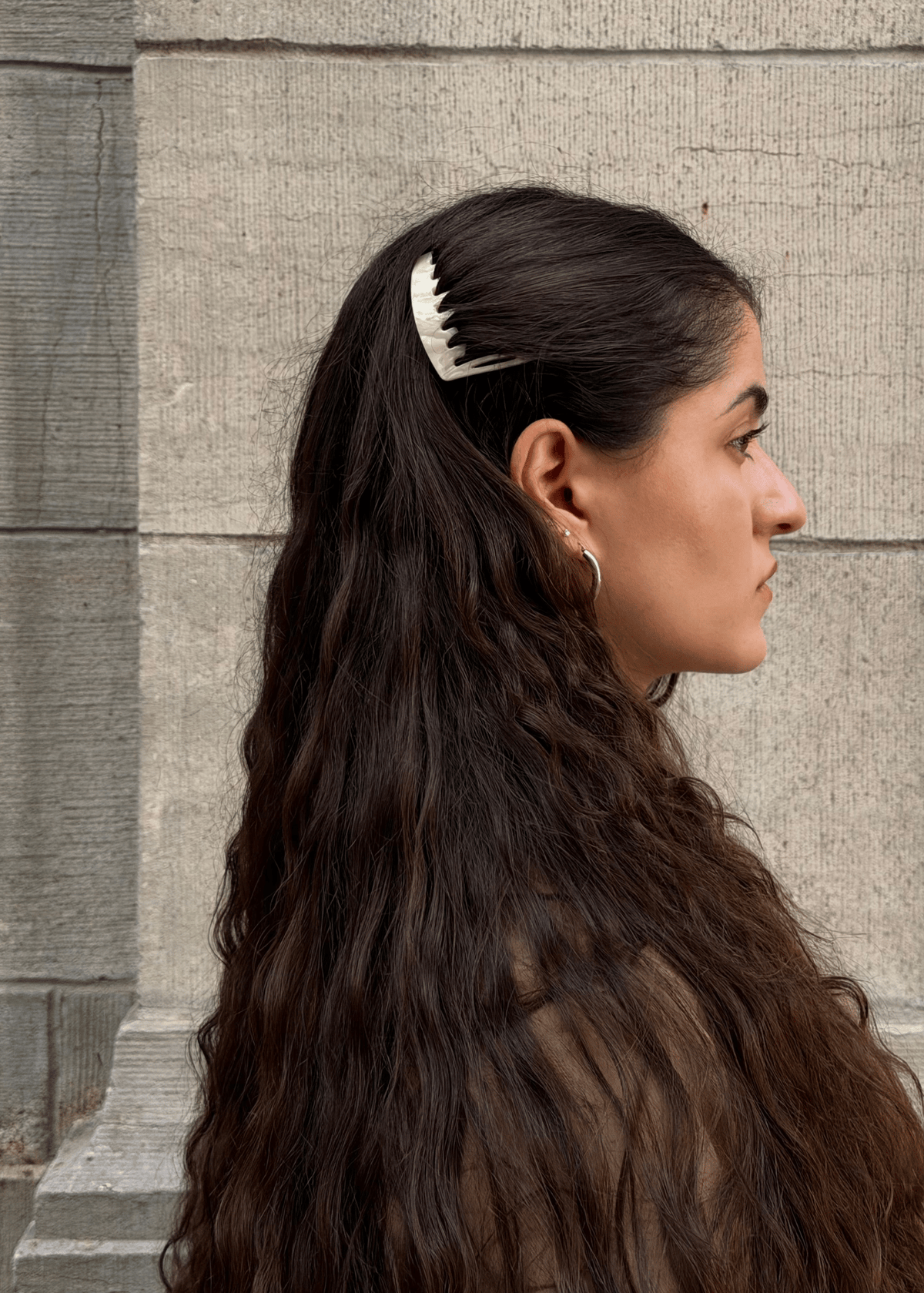 A woman with long, wavy hair swept back from her face using a light neutral hair comb.