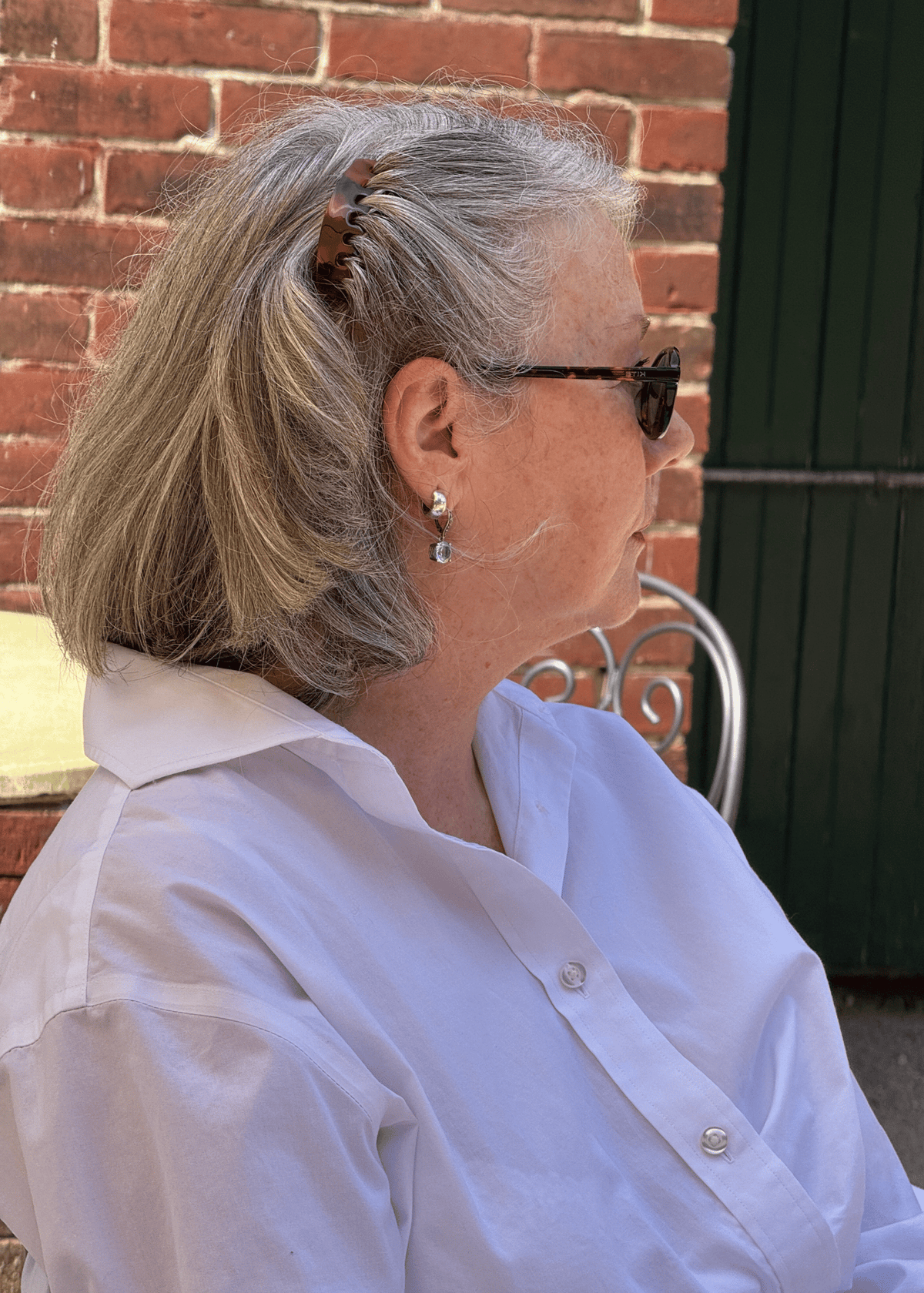 A mature woman in profile with jaw-length grey hair. The side of her hair is swept back from her face with a tortoiseshell hair comb. 