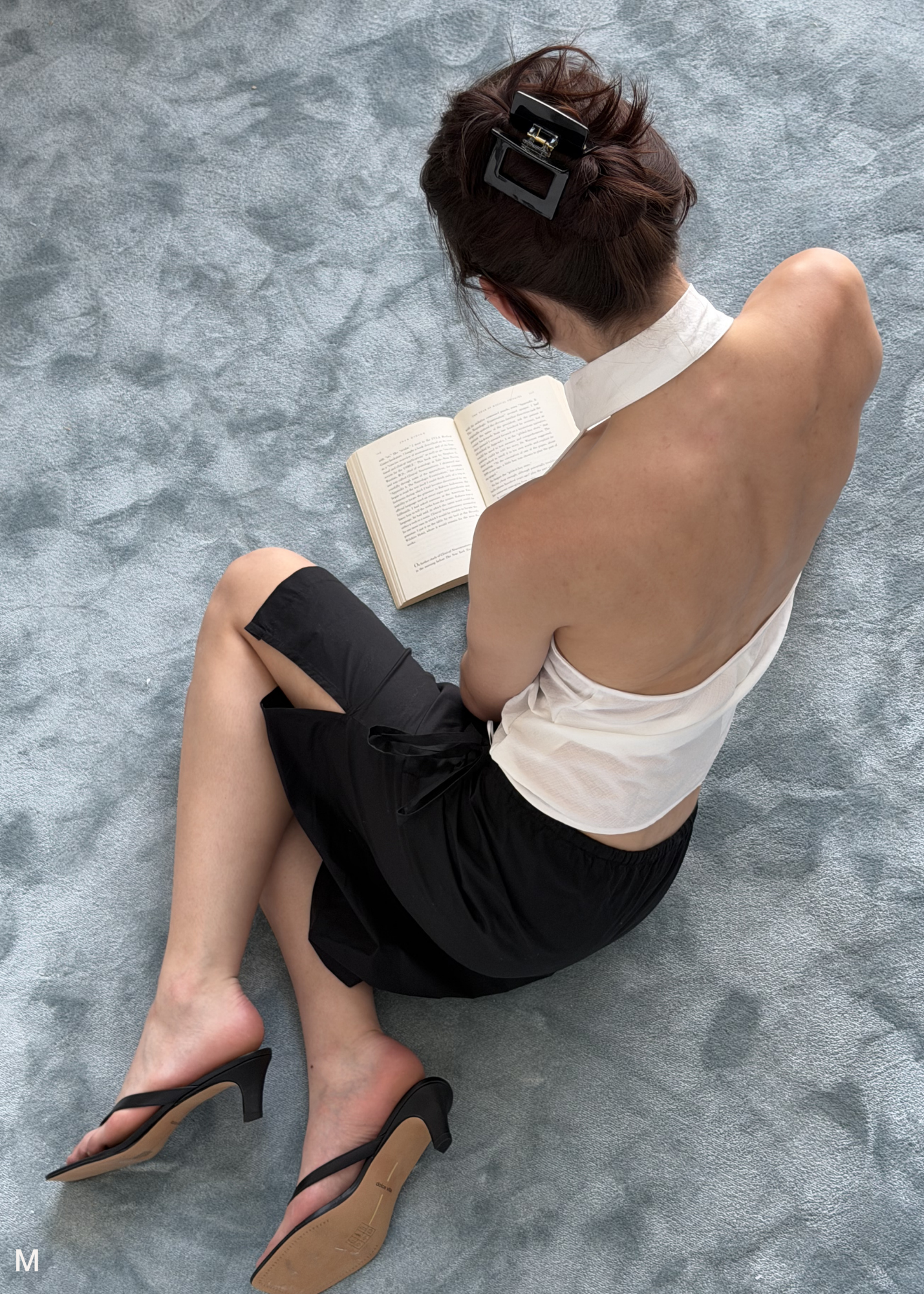 Person sitting on a textured floor reading with a black hair clip in their hair.