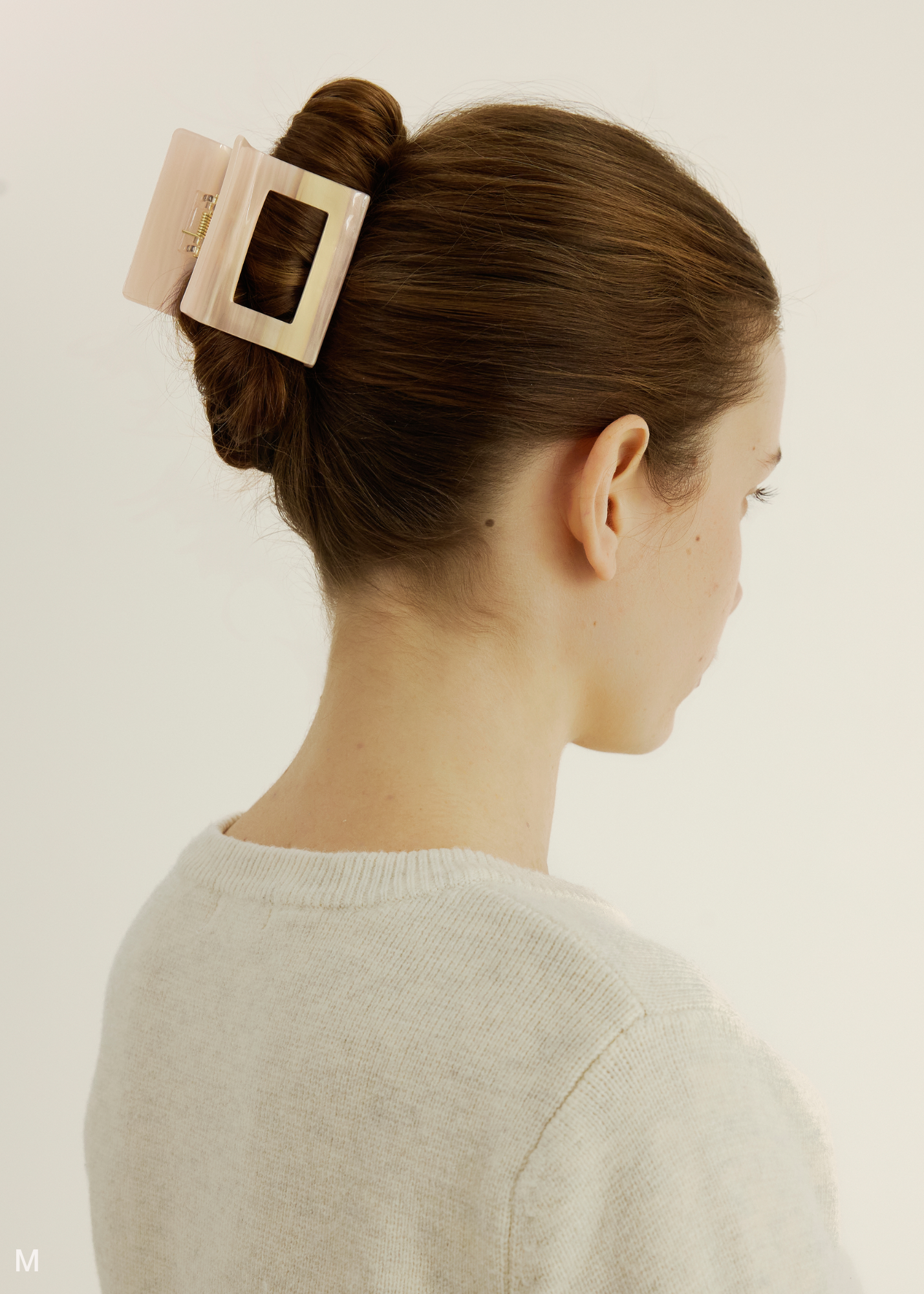 Woman with a hair bun secured by a pink hair clip on a plain background